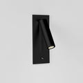This Clérachic reading light in matt black, lit, mounted on a plain white wall, head angled down.
