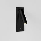 This Clérachic reading light in matt black, lit, mounted on a plain white wall, head angled down.