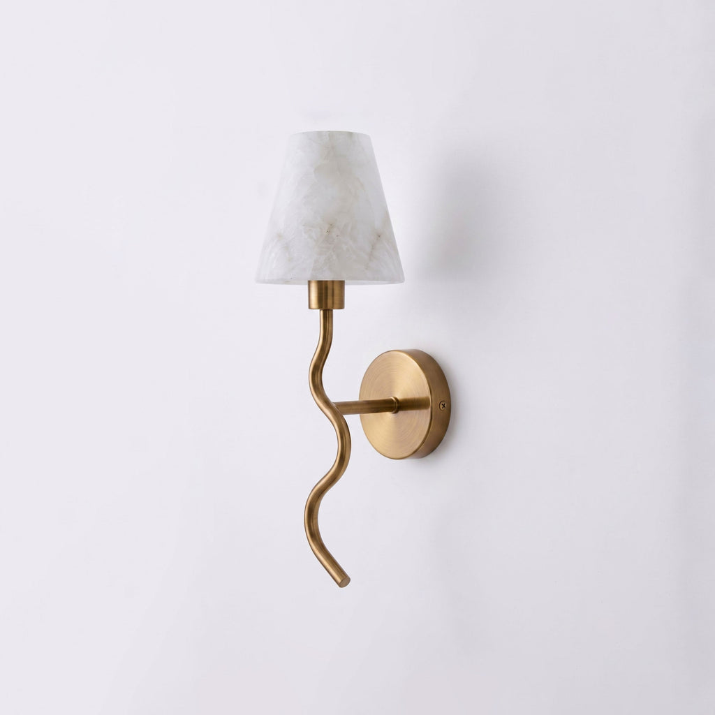 Front-on against a plain backdrop, the curling brushed brass arm of this Clérachic wall sconce winds down from its white cone shade, unlit.