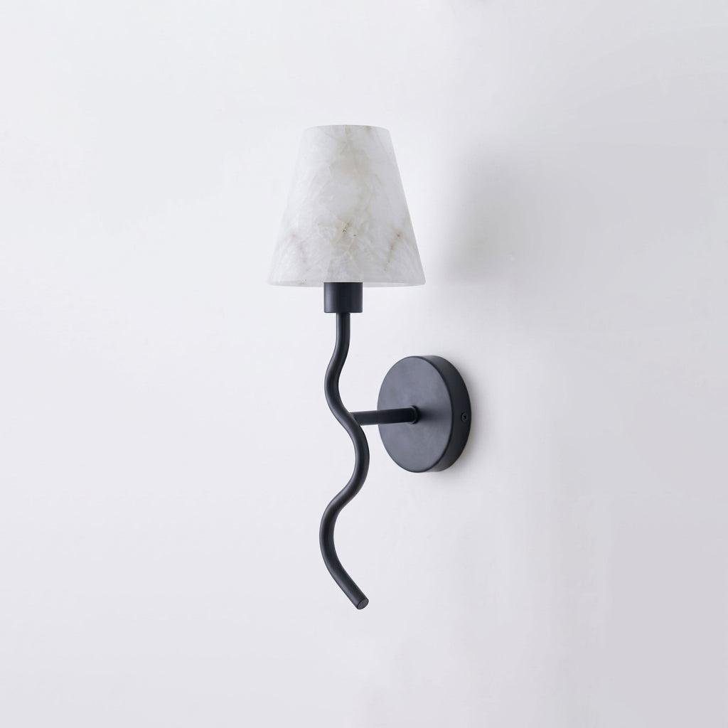 Angled on a plain backdrop, this Clérachic wall sconce shows its matte black finish, serpentine arm and white cone shade, unlit.
