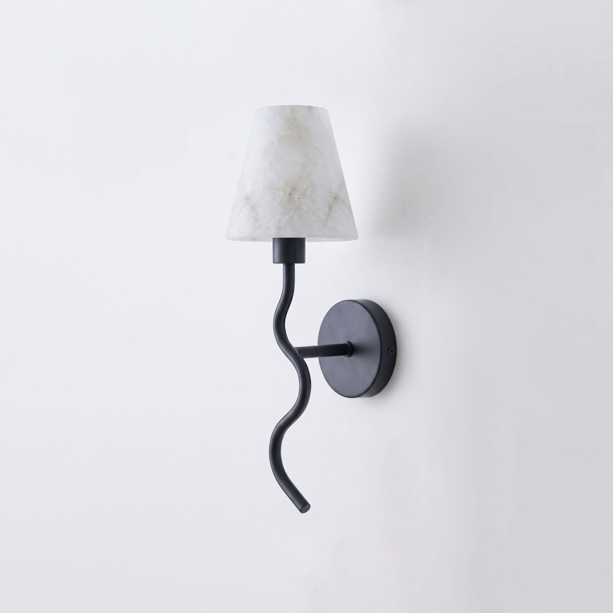 Angled on a plain backdrop, this Clérachic wall sconce shows its matte black finish, serpentine arm and white cone shade, unlit.