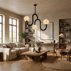Above a low coffee table and built-in bookshelves, the black-finish chandelier from Clérachic lights a neutral living room.