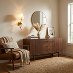 Beside a round mirror over a console with a pampas grass arrangement, this Clérachic wall sconce in brushed brass warms a lit corner near a leather armchair.