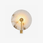 Studio view of this Clérachic wall sconce in brushed brass, its alabaster disc lit warm against a white backdrop.
