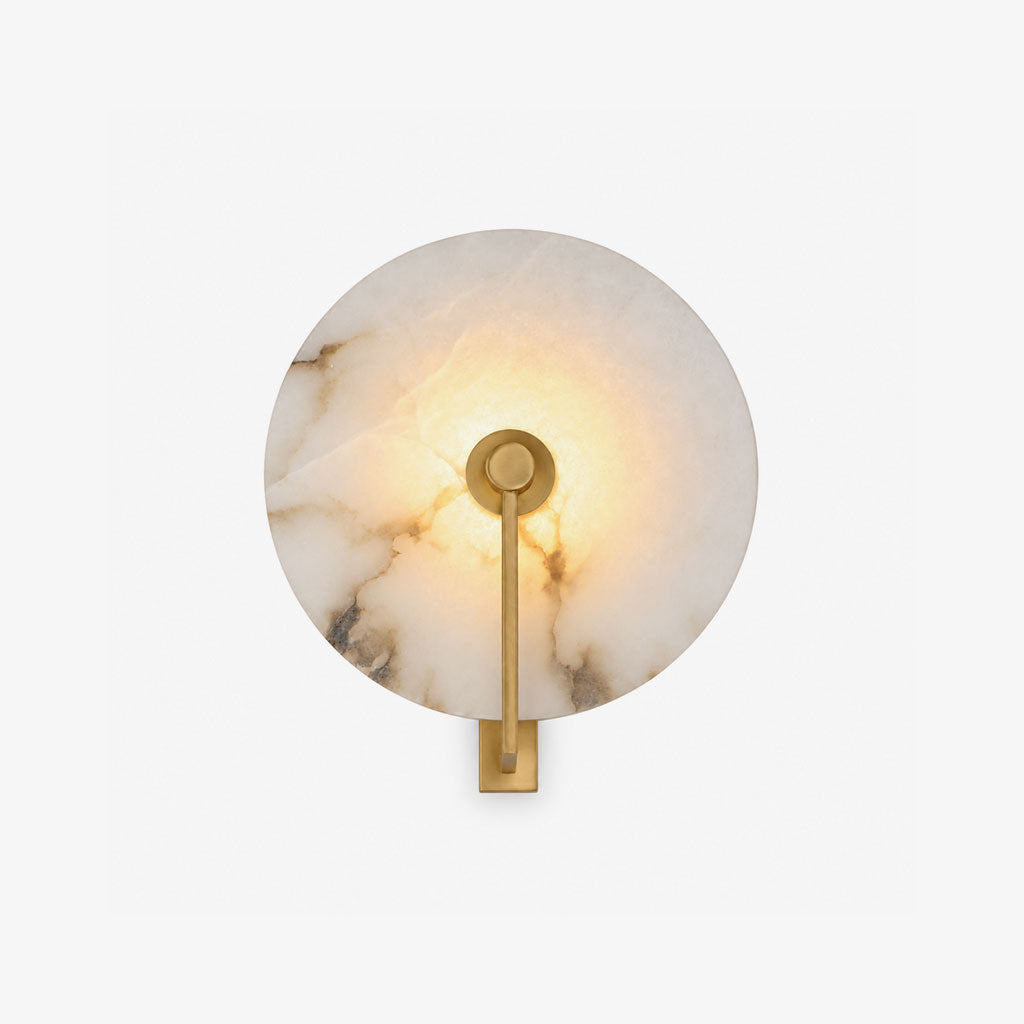 Studio view of this Clérachic wall sconce in brushed brass, its alabaster disc lit warm against a white backdrop.