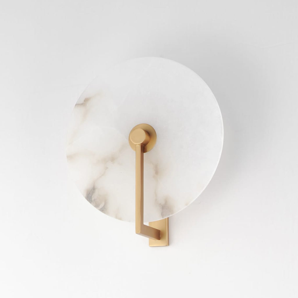 This Clérachic wall sconce in brushed brass shows its angular arm crossing the alabaster disc's veined face.