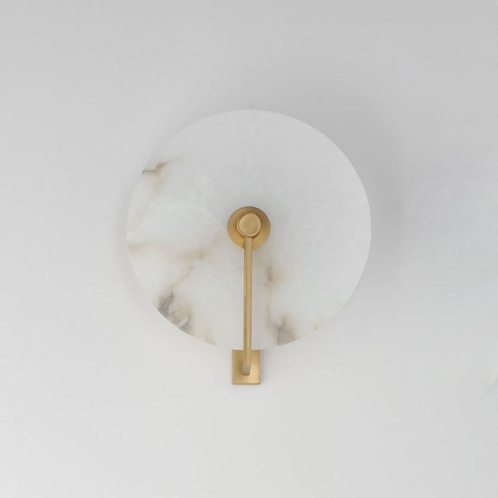 Studio shot of this Clérachic wall sconce in brushed brass, the arm mounted straight down the disc's centre.