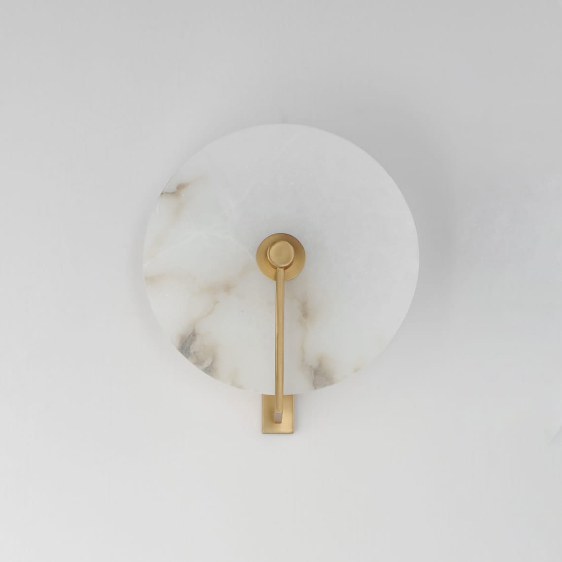 Studio shot of this Clérachic wall sconce in brushed brass, the arm mounted straight down the disc's centre.