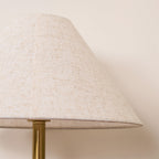 Close-up of the Clérachic lamp's cream fabric shade edge and brass pole against a plain wall.