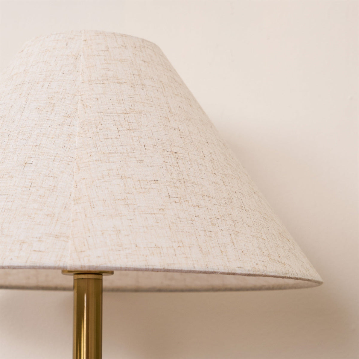 Close-up of the Clérachic lamp's cream fabric shade edge and brass pole against a plain wall.