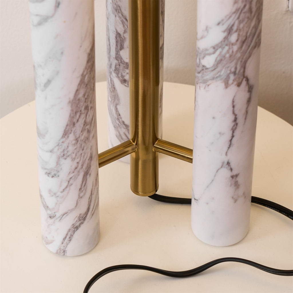 Overhead close-up of the Clérachic lamp's marble columns and brass joints on the round tabletop, cord below.