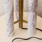 Overhead close-up of the Clérachic lamp's marble columns and brass joints on the round tabletop, cord below.