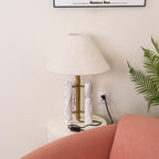Clérachic table lamp with the wall socket and cord visible again, framed print above and fern beside the shade.