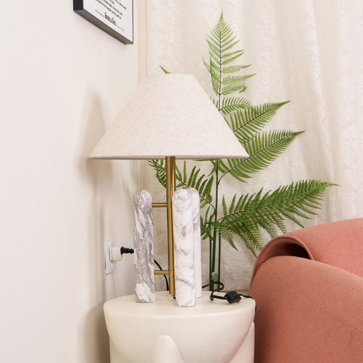 Clérachic table lamp's cord runs down to a wall socket beside a sheer curtain, fern leaning in from the right.