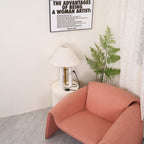 Clérachic table lamp lit in the room corner, a framed print on the wall above and the coral armchair filling the foreground.