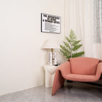 Wider shot of the same corner: Clérachic table lamp, framed print and fern, with the armchair reduced to a sliver at the edge.