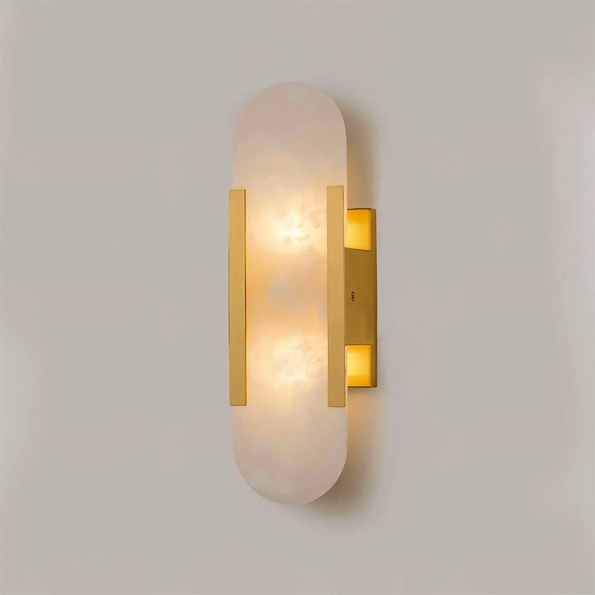 Clérachic brass Olraeia Alabaster Wall Sconce lit head-on, warm light pooling through the veined capsule panel