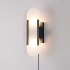 Black-finish Kristy alabaster wall lamp lit on a pale wall, its plug-in power cord running down below