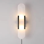 Tall Kristy alabaster sconce in black, lit head-on with the plug-in cord dropping from the base