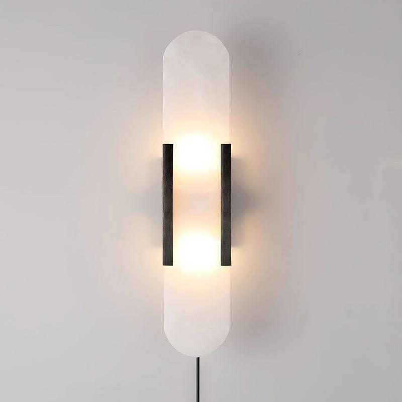 Tall Kristy alabaster sconce in black, lit head-on with the plug-in cord dropping from the base