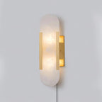 Angled view of the brass Kristy sconce, showing the open glow slots above and below its backplate