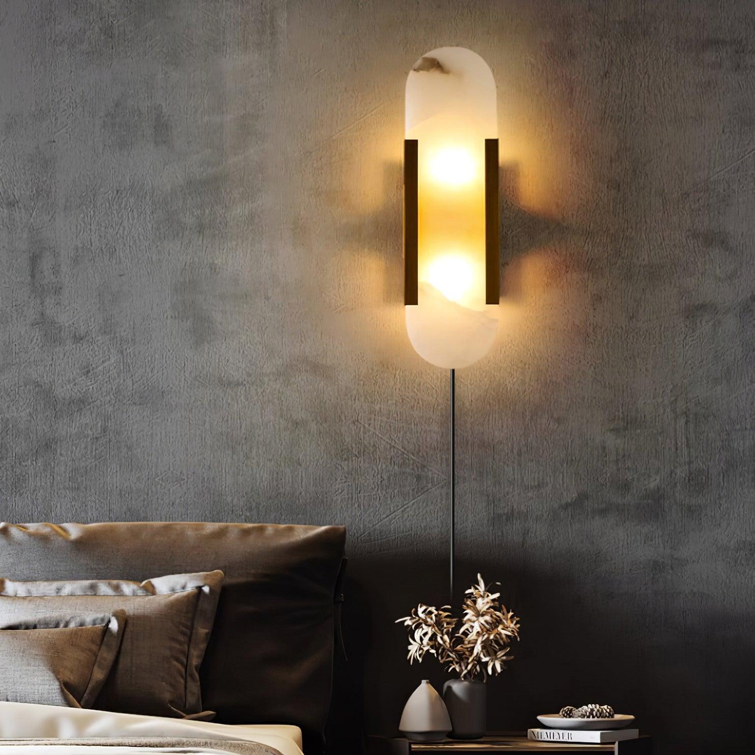 Brass Kristy sconce lit on a raw concrete bedroom wall, long cord dropping to the nightstand