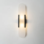Clérachic black Olraeia sconce lit on a pale plaster wall, the stone panel's soft cloudy grain showing through