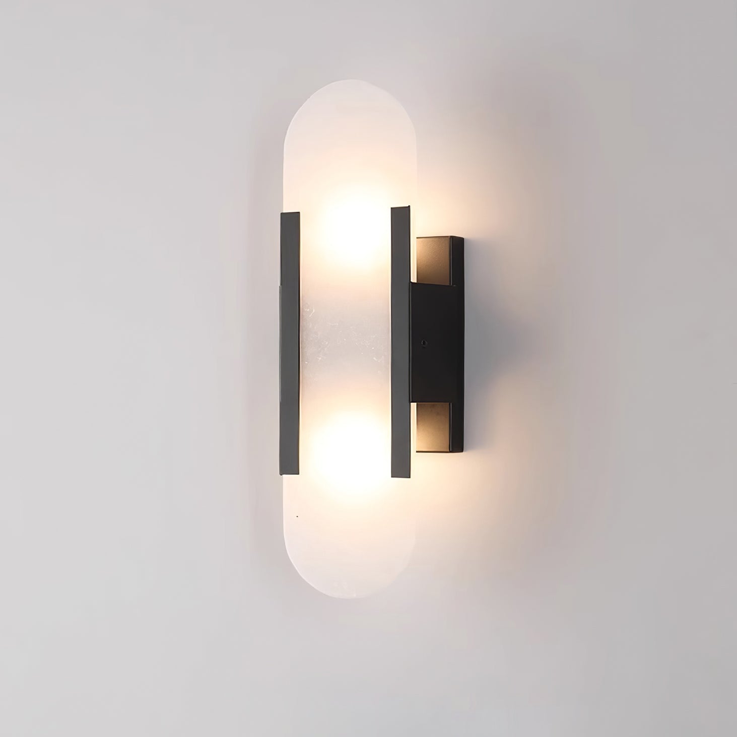 Clérachic olraeia Alabaster Wall Sconce in black, lit from within, its capsule stone panel glowing on a grey wall