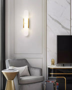 Clérachic brass Olraeia sconce on a panelled living-room wall next to a grey velvet armchair and marble surround