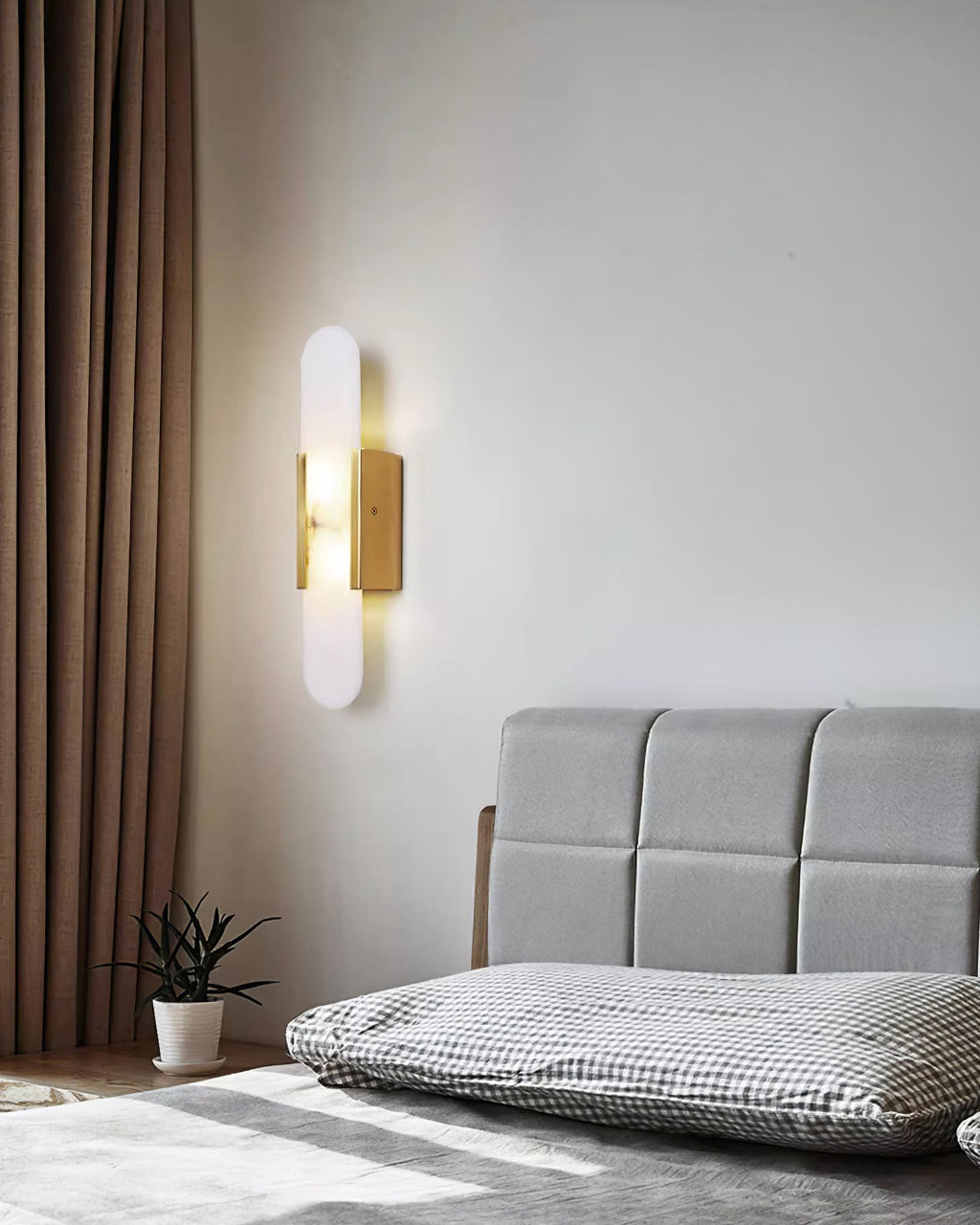 Clérachic brass Olraeia sconce beside heavy curtains in a bedroom, lighting the corner above a potted plant