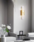 Clérachic olraeia sconce lit beside an ornate plaster arch in a pale living room with grey sofas and daisies