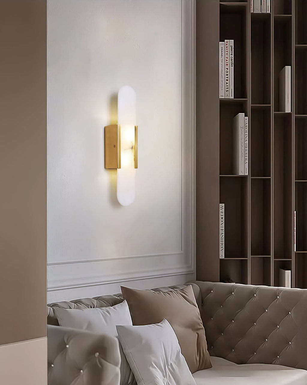 Clérachic olraeia sconce glowing on a white living-room wall above a tufted sofa, tall bookshelves alongside