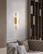 Clérachic olraeia sconce glowing on a white living-room wall above a tufted sofa, tall bookshelves alongside