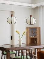 Two single Clérachic pendants glow above a dark wood dining table with mixed wood and upholstered chairs.