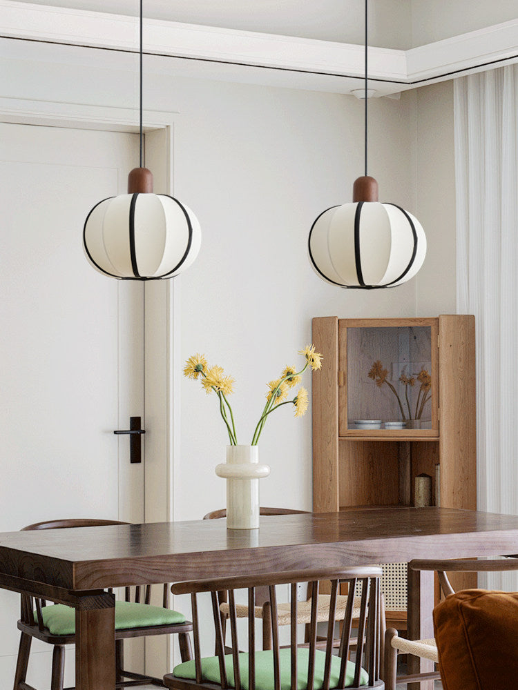 Two single Clérachic pendants glow above a dark wood dining table with mixed wood and upholstered chairs.