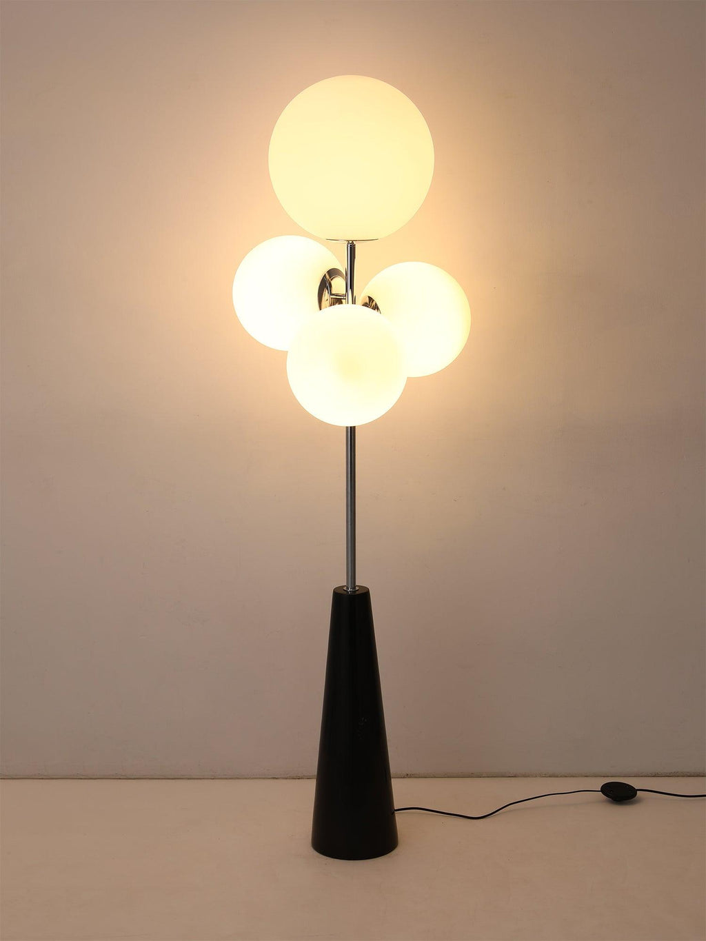 A softer-lit variant of the same dark backdrop shot, the Clérachic floor lamp's frosted white globes glowing on their chrome mount.