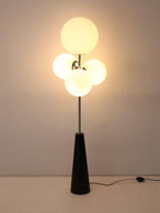 A softer-lit variant of the same dark backdrop shot, the Clérachic floor lamp's frosted white globes glowing on their chrome mount.