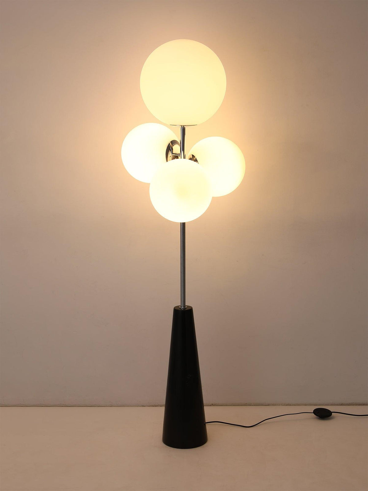 A softer-lit variant of the same dark backdrop shot, the Clérachic floor lamp's frosted white globes glowing on their chrome mount.