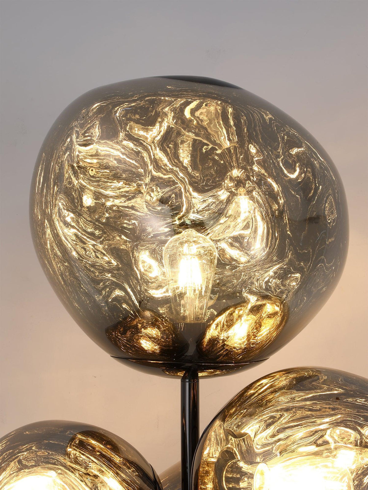 Close-up of one lit smoke-glass globe on this Clérachic floor lamp, its swirled marbled texture glowing around the visible filament bulb.