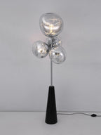 Clérachic floor lamp lit against a plain grey studio backdrop, its marbled smoke-glass globes glowing above the visible black power cord.