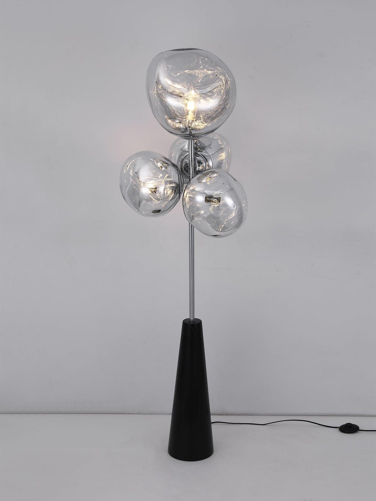 Clérachic floor lamp lit against a plain grey studio backdrop, its marbled smoke-glass globes glowing above the visible black power cord.
