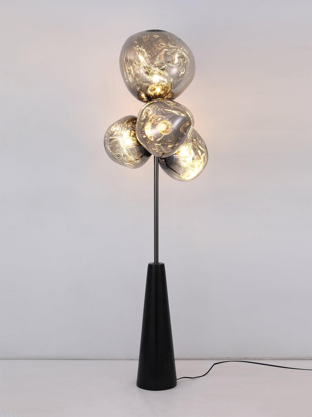 Clérachic floor lamp lit front-on against a plain white backdrop, warm light glowing through its four marbled smoke-glass globes.
