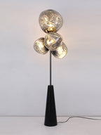 Clérachic floor lamp lit front-on against a plain white backdrop, warm light glowing through its four marbled smoke-glass globes.