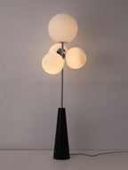 Frosted white globes glow warmly on this Clérachic floor lamp, photographed against a dark, moody backdrop with the cord trailing to the floor.