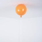 A single orange Clérachic balloon light hangs close against a plain white ceiling-wall corner.