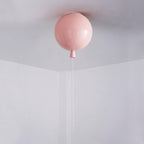 A single pink Clérachic balloon light hangs from a plain white ceiling corner, its pull cord reaching down.