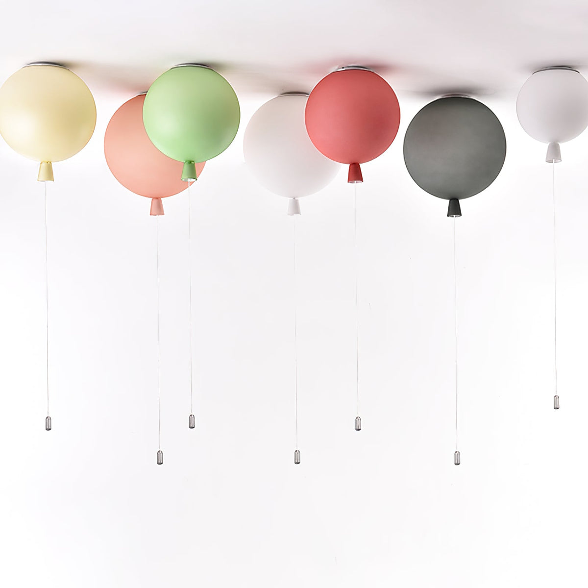 Six Clérachic balloon lights in muted cream, pink, sage, white, dusty rose and charcoal hang together with pull cords showing.