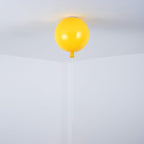A single yellow Clérachic balloon light hangs from a plain white ceiling corner with its pull cord below.