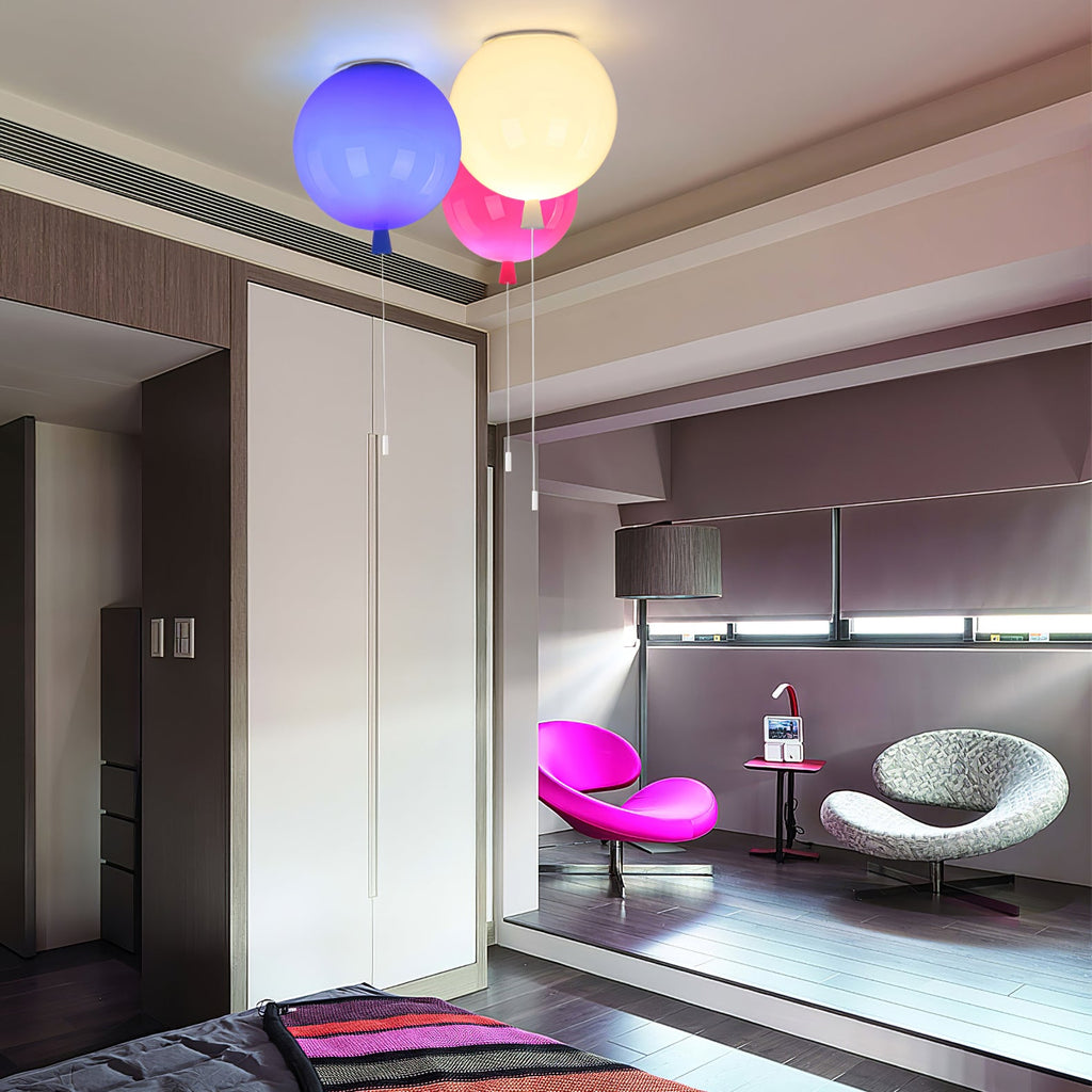 In a modern bedroom with a pink armchair, three Clérachic balloon lights in blue, white and pink hang near a wardrobe.