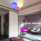 In a modern bedroom with a pink armchair, three Clérachic balloon lights in blue, white and pink hang near a wardrobe.